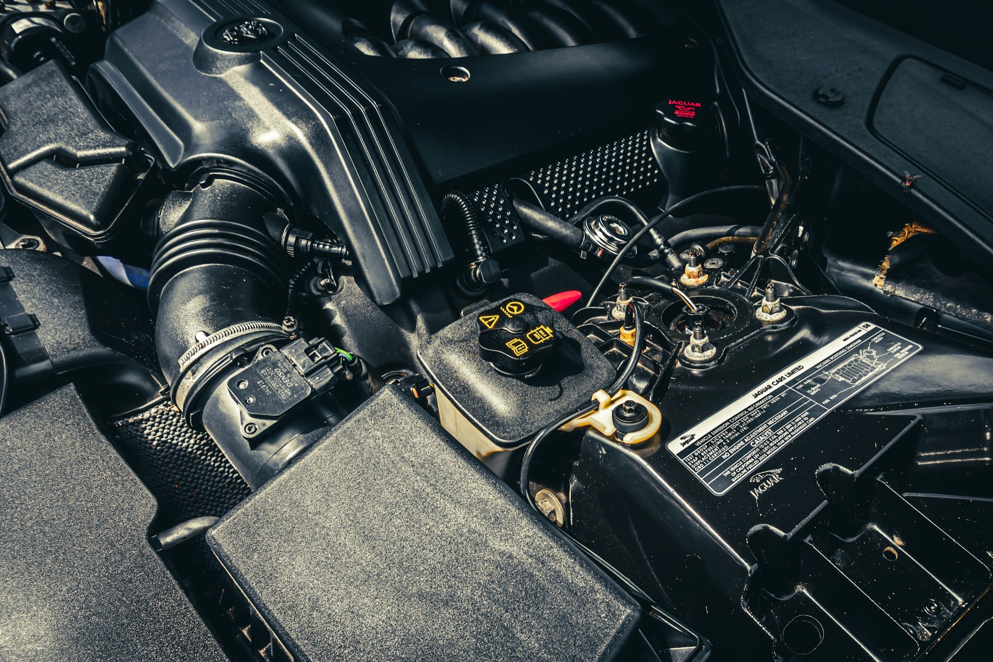 A car battery with yellow terminal covers under an open hood