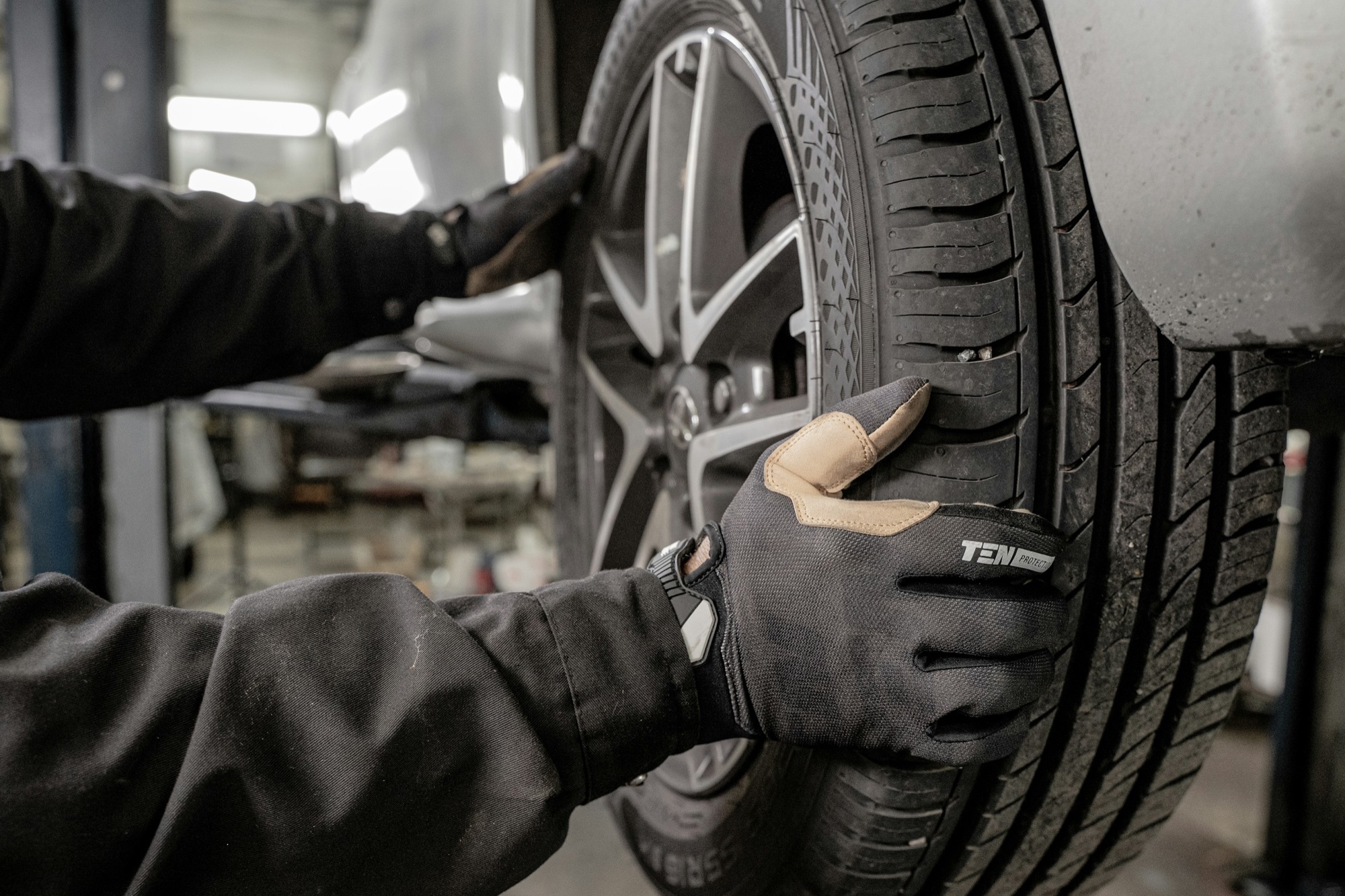 A mechanic in work gloves fitting a tire onto a car in a repair bay